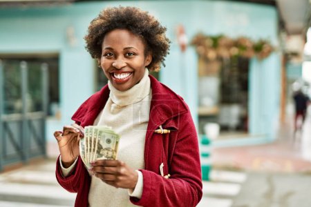 Foto de Joven mujer afroamericana sosteniendo billetes de banco en dólares en la ciudad - Imagen libre de derechos