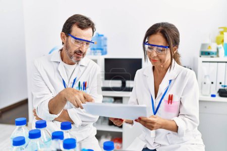 Photo for Middle age man and woman partners wearing scientist uniform reading document at laboratory - Royalty Free Image