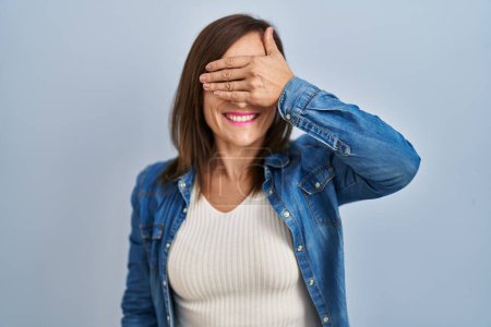 Photo for Middle age brunette woman wearing casual denim jacket over isolated background smiling and laughing with hand on face covering eyes for surprise. blind concept. - Royalty Free Image