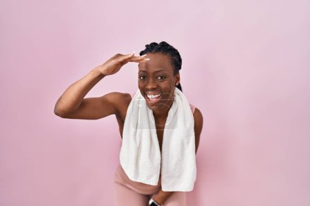 Photo for Beautiful black woman wearing sportswear and towel over pink background very happy and smiling looking far away with hand over head. searching concept. - Royalty Free Image