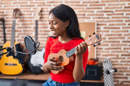 Foto de Joven afroamericana mujer músico jugando ukelele en estudio de música - Imagen libre de derechos