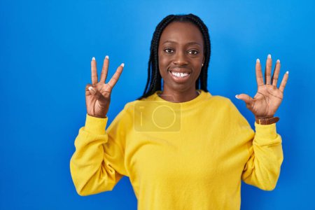 Photo for Beautiful black woman standing over blue background showing and pointing up with fingers number eight while smiling confident and happy. - Royalty Free Image