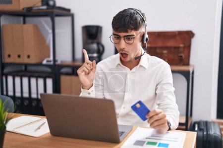 Photo for Young hispanic man working using computer laptop holding credit card surprised pointing with finger to the side, open mouth amazed expression. - Royalty Free Image