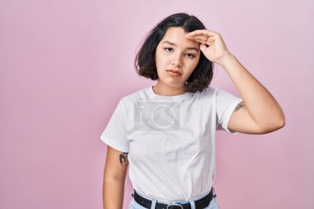 Photo for Young hispanic woman wearing casual white t shirt over pink background worried and stressed about a problem with hand on forehead, nervous and anxious for crisis - Royalty Free Image