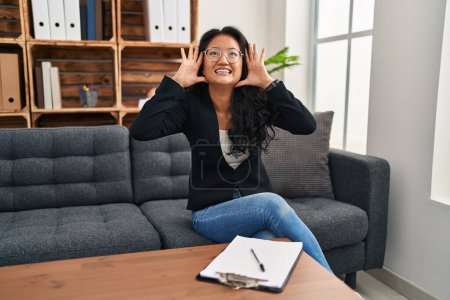 Photo for Young asian woman at consultation office smiling cheerful playing peek a boo with hands showing face. surprised and exited - Royalty Free Image