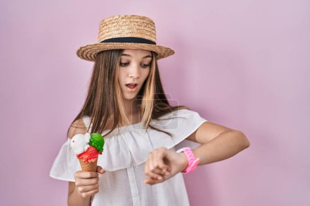 Téléchargez les photos : Teenager girl holding ice cream looking at the watch time worried, afraid of getting late - en image libre de droit