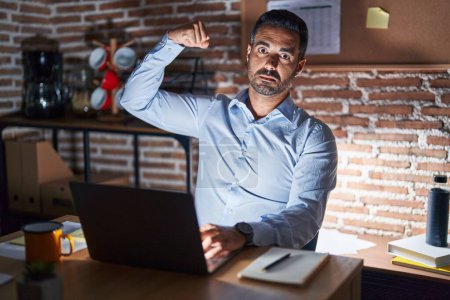 Photo for Hispanic man with beard working at the office at night strong person showing arm muscle, confident and proud of power - Royalty Free Image
