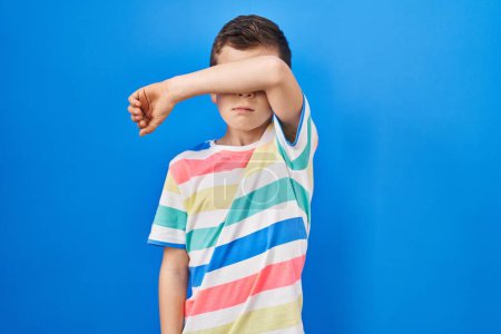 Téléchargez les photos : Young caucasian kid standing over blue background covering eyes with arm, looking serious and sad. sightless, hiding and rejection concept - en image libre de droit
