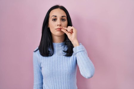 Photo for Hispanic woman standing over pink background mouth and lips shut as zip with fingers. secret and silent, taboo talking - Royalty Free Image