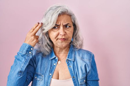 Photo for Middle age woman with grey hair standing over pink background shooting and killing oneself pointing hand and fingers to head like gun, suicide gesture. - Royalty Free Image