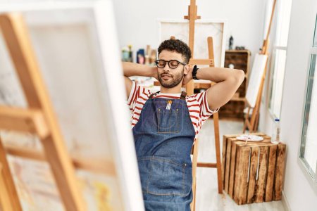 Téléchargez les photos : Jeune artiste arabe homme détendu avec les mains sur la tête au studio d'art. - en image libre de droit