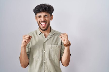 Téléchargez les photos : Homme arabe avec barbe debout sur fond blanc excité pour le succès avec les bras levés et les yeux fermés célébrant la victoire en souriant. concept gagnant. - en image libre de droit
