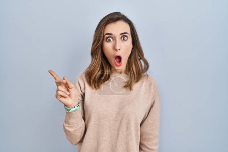 Photo for Young woman standing over isolated background surprised pointing with finger to the side, open mouth amazed expression. - Royalty Free Image