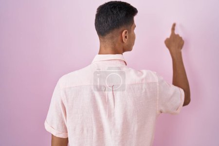 Photo for Young hispanic man standing over pink background posing backwards pointing ahead with finger hand - Royalty Free Image