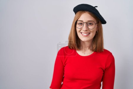 Téléchargez les photos : Jeune femme rousse debout portant des lunettes et un béret avec un sourire heureux et cool sur le visage. chanceux. - en image libre de droit