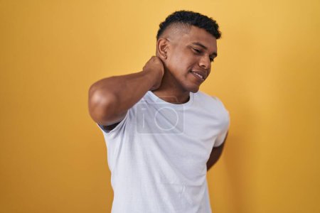 Photo for Young hispanic man standing over yellow background suffering of neck ache injury, touching neck with hand, muscular pain - Royalty Free Image