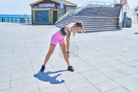Photo for Young blonde woman wearing sportswear stretching at seaside - Royalty Free Image