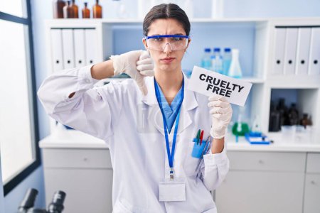 Foto de Young beautiful woman working on cruelty free laboratory with angry face, negative sign showing dislike with thumbs down, rejection concept - Imagen libre de derechos