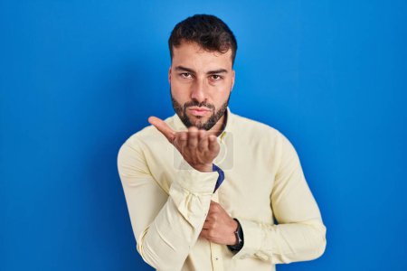 Photo for Handsome hispanic man standing over blue background looking at the camera blowing a kiss with hand on air being lovely and sexy. love expression. - Royalty Free Image