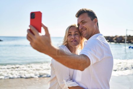 Téléchargez les photos : Middle age man and woman couple hugging each other make selfie by the smartphone at seaside - en image libre de droit