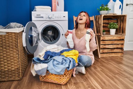 Photo for Young caucasian woman doing laundry holding socks angry and mad screaming frustrated and furious, shouting with anger looking up. - Royalty Free Image