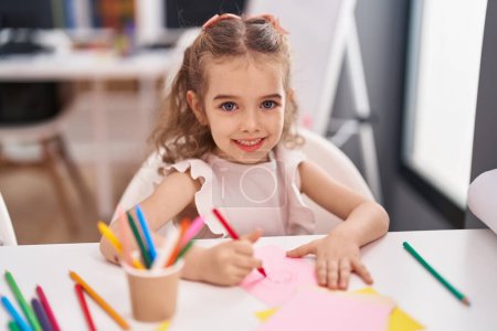 Photo for Adorable caucasian girl student sitting on table drawing on paper at classroom - Royalty Free Image