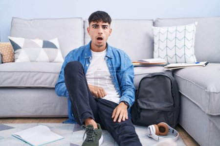 Photo for Young hispanic man sitting on the floor studying for university afraid and shocked with surprise and amazed expression, fear and excited face. - Royalty Free Image