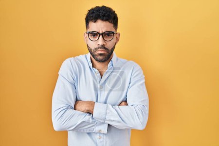 Photo for Hispanic man with beard standing over yellow background skeptic and nervous, disapproving expression on face with crossed arms. negative person. - Royalty Free Image