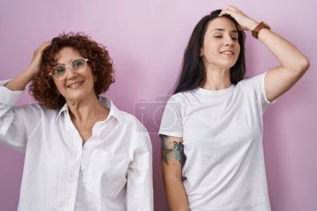 Téléchargez les photos : Mère et fille hispaniques portant un t-shirt blanc décontracté sur fond rose souriant cheveux touchants confiants avec geste de la main vers le haut, posant attrayant et à la mode - en image libre de droit