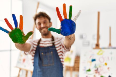 Photo for Young hispanic man smiling confident showing colored palm hands at art studio - Royalty Free Image