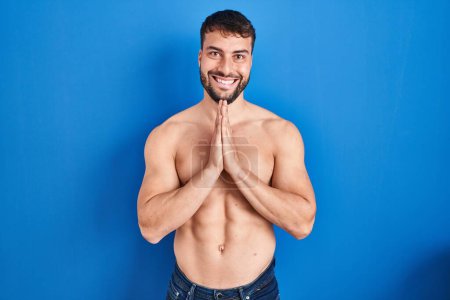 Téléchargez les photos : Bel homme hispanique debout torse nu priant avec les mains ensemble demandant pardon souriant confiant. - en image libre de droit