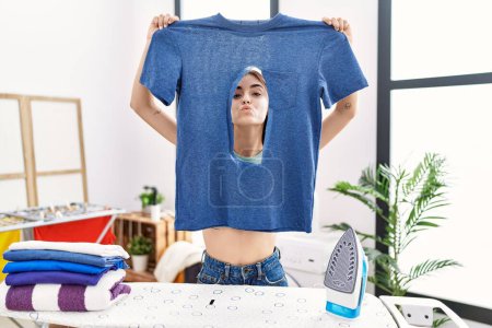 Photo for Young hispanic woman ironing holding burned iron shirt at laundry room looking at the camera blowing a kiss being lovely and sexy. love expression. - Royalty Free Image