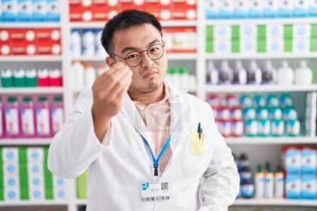 Foto de Chinese young man working at pharmacy drugstore doing italian gesture with hand and fingers confident expression - Imagen libre de derechos