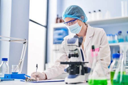 Téléchargez les photos : Young blonde woman wearing scientist uniform and medical mask using microscope at laboratory - en image libre de droit
