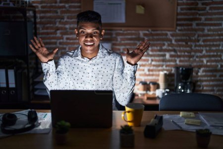 Téléchargez les photos : Jeune homme hispanique travaillant au bureau la nuit célébrant fou et étonné pour le succès avec les bras levés et les yeux ouverts hurlant excité. concept gagnant - en image libre de droit