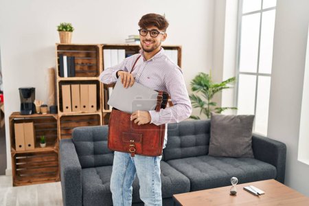 Foto de Young arab man psychologist smiling confident holding laptop at psychology center - Imagen libre de derechos