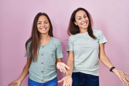 Téléchargez les photos : Jeune mère et fille debout sur fond rose souriant gai avec les bras ouverts comme accueil amical, salutations positives et confiantes - en image libre de droit