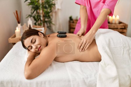 Téléchargez les photos : Jeune belle femme hispanique allongée sur la table ayant des pierres chaudes massage au salon de beauté - en image libre de droit