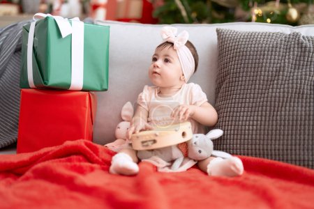 Photo for Adorable toddler playing tambourine sitting on sofa by christmas tree at home - Royalty Free Image