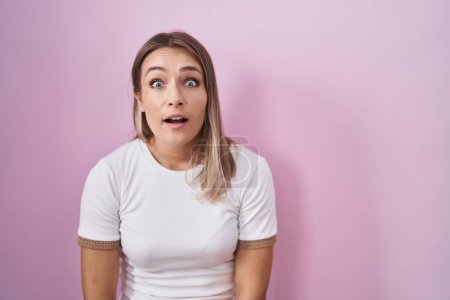 Photo for Blonde caucasian woman standing over pink background afraid and shocked with surprise and amazed expression, fear and excited face. - Royalty Free Image