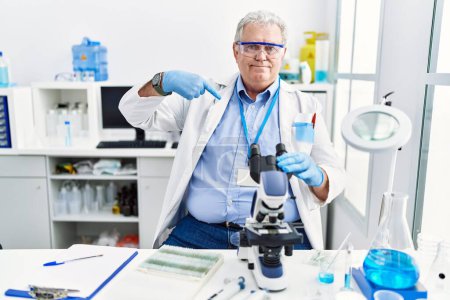 Foto de Hombre caucásico mayor trabajando en laboratorio científico mirando confiado con sonrisa en la cara, señalándose con los dedos orgullosos y felices. - Imagen libre de derechos