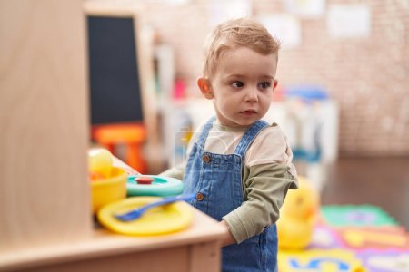 Téléchargez les photos : Adorable tout-petit jouant avec la cuisine de jeu debout à la maternelle - en image libre de droit