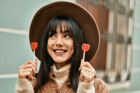 Photo for Brunette woman wearing winter hat being funny holding lollipops outdoors at the city - Royalty Free Image
