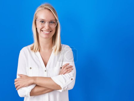 Téléchargez les photos : Young caucasian woman standing over blue background happy face smiling with crossed arms looking at the camera. positive person. - en image libre de droit