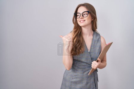 Téléchargez les photos : Caucasian woman wearing glasses and business clothes pointing to the back behind with hand and thumbs up, smiling confident - en image libre de droit