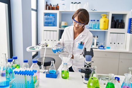 Photo for Young beautiful hispanic woman scientist pouring liquid on bottle at laboratory - Royalty Free Image