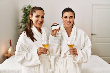 Téléchargez les photos : Deux femmes portant un toast à la carte de crédit avec champagne debout au centre de beauté - en image libre de droit