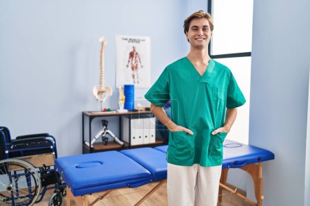 Téléchargez les photos : Young caucasian man pysiotherapist smiling confident standing at rehab clinic - en image libre de droit
