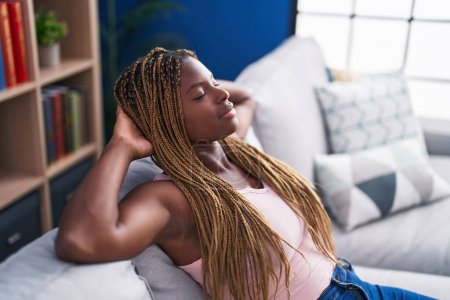 Foto de Mujer afroamericana relajada con las manos en la cabeza sentada en el sofá en casa - Imagen libre de derechos