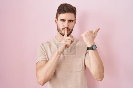 Téléchargez les photos : Hispanic man with beard standing over pink background asking to be quiet with finger on lips pointing with hand to the side. silence and secret concept. - en image libre de droit